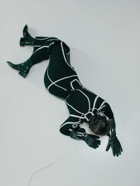 Overhead shot of a Black woman in a black and white catsuit and black boots on a white surface, showcasing fashion and style.