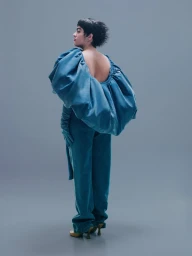 Model in voluminous blue top and matching trousers looking back against a grey studio seamless background