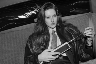 Black and white portrait of a woman in a leather jacket holding a portable radio inside a car