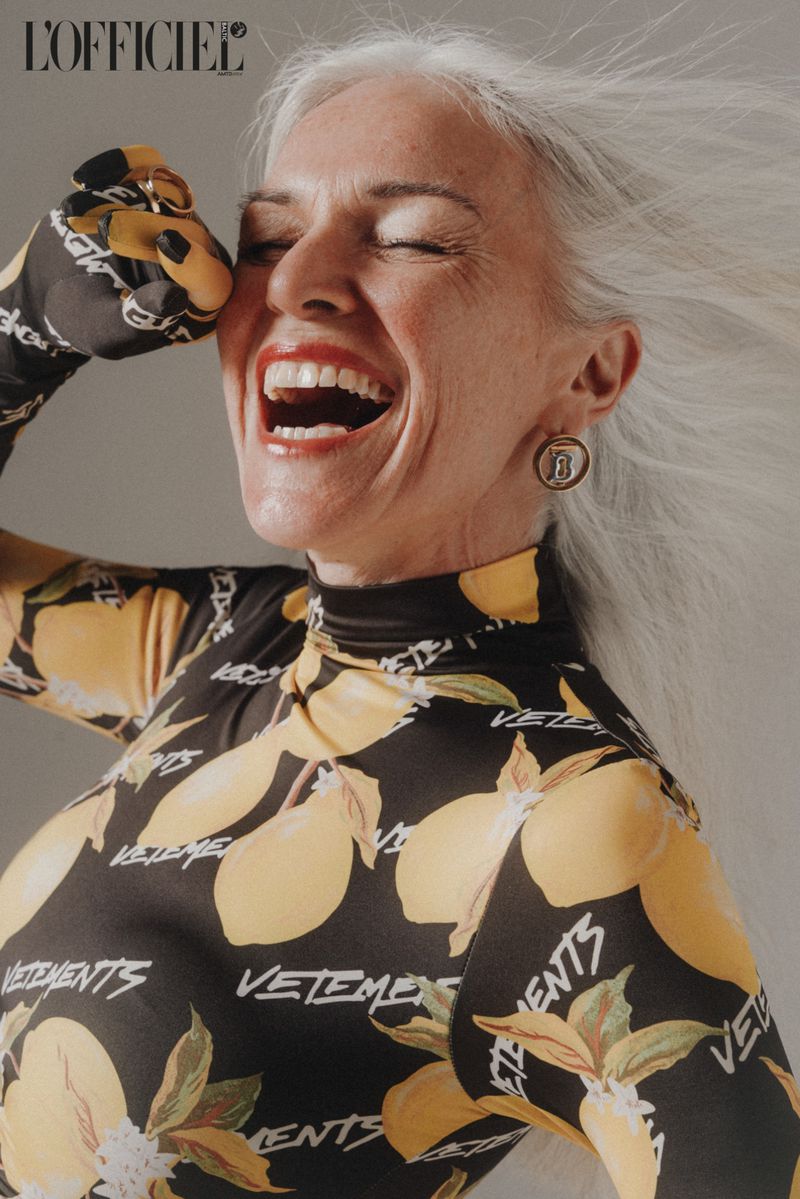 Close-up shot of a smiling mature woman with grey hair, an open mouth, and a printed top, capturing a joyful moment.