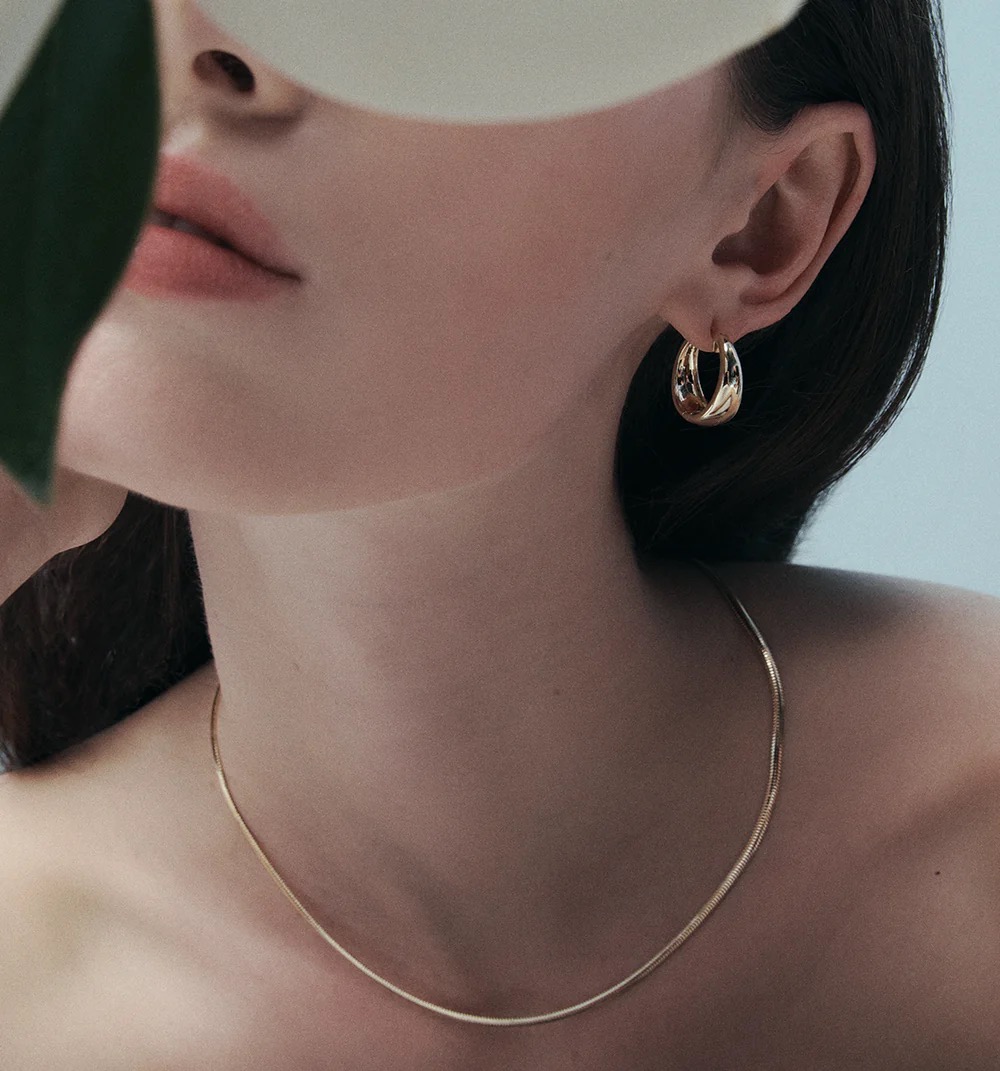 Close-up of a woman wearing a gold necklace and earrings, soft lighting, and a minimalist aesthetic highlighting beauty and fashion.