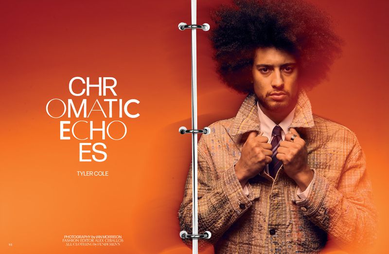 Portrait of Tyler Cole with afro, wearing a patterned coat, shirt and tie against an orange gradient backdrop in a fashion editorial shot.