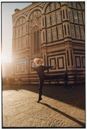 Model leaping in mid-air in front of an ornate historical stone building during golden hour