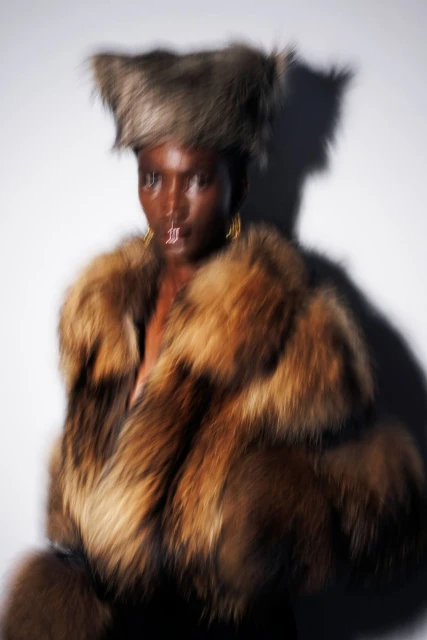 Fashion shot of an African American woman wearing a furry hat and a brown fur coat against a plain white backdrop, fashion, style, elegance.