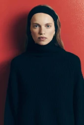 Model wearing a black turtleneck sweater and black headband against a vibrant red background.