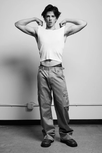 Full body shot of an adult male model wearing a white tank top and khaki cargo pants in a photo studio against a white background.