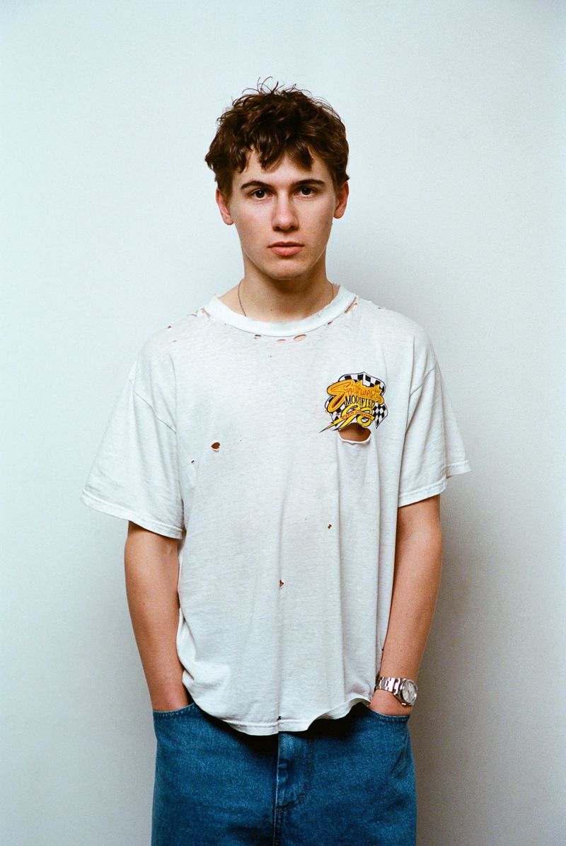 Actor Sam Nivola wearing a distressed white t-shirt and blue jeans against a neutral backdrop for HERO Magazine.