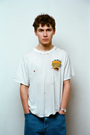 Actor Sam Nivola wearing a distressed white t-shirt and blue jeans against a neutral backdrop for HERO Magazine.