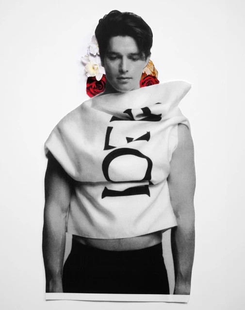 Monochromatic fashion shot of a man in a graphic top and dark pants, adorned with flowers against a stark white background.