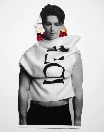 Monochromatic fashion shot of a man in a graphic top and dark pants, adorned with flowers against a stark white background.