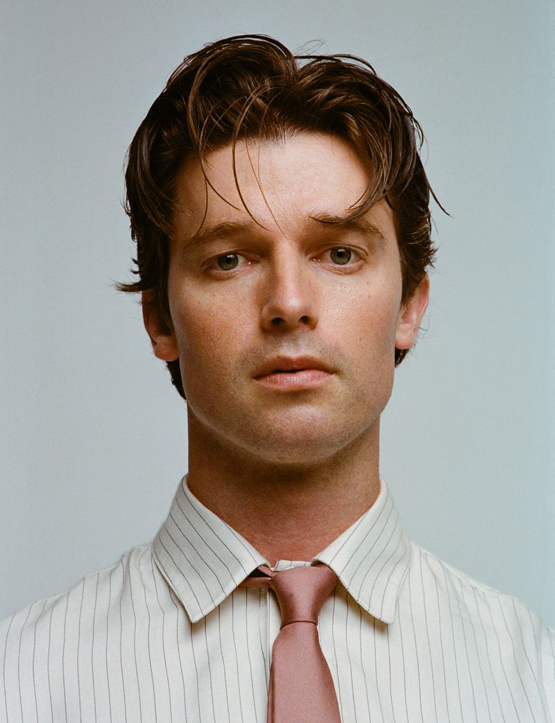 Portrait of actor Patrick Schwarzenegger wearing a pinstripe shirt and tie against a plain light background
