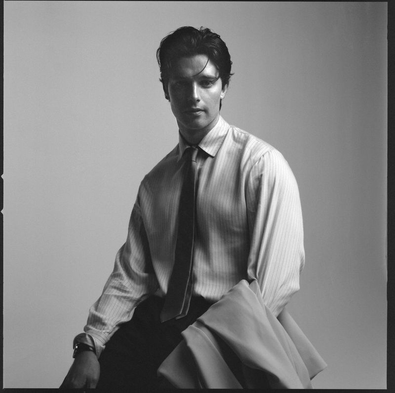 Portrait of Patrick Schwarzenegger wearing a striped shirt and tie against a plain studio background for HERO Magazine.