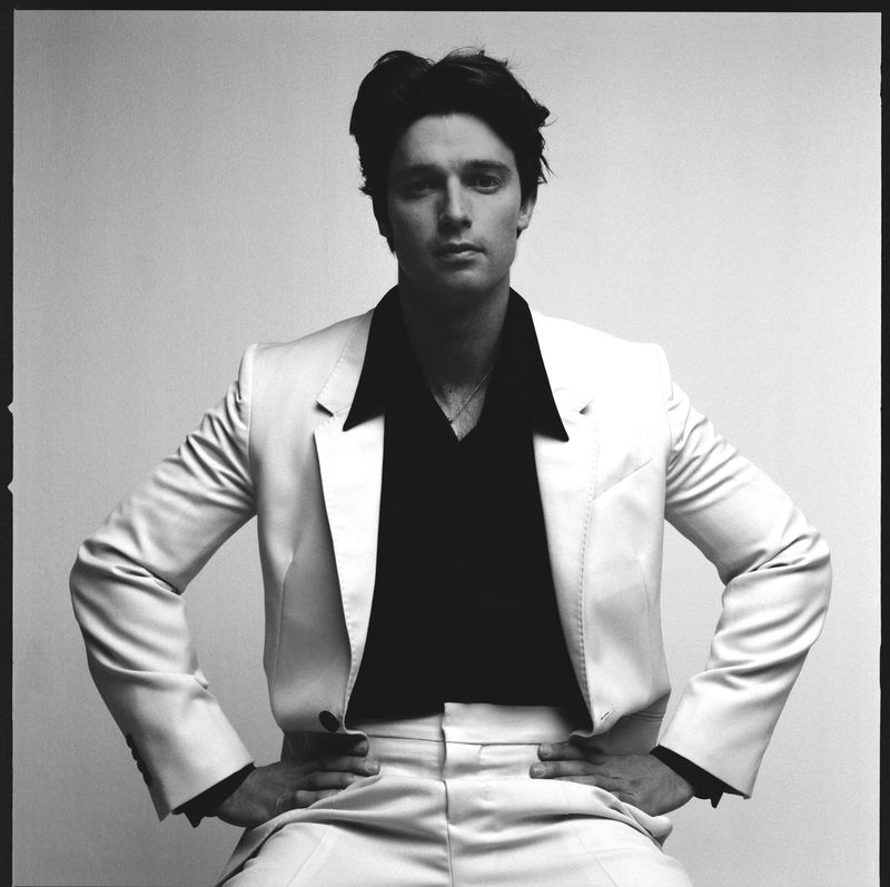 Portrait of an adult male in a suit and button-down shirt, posing in front of a neutral background, photographed in black and white.