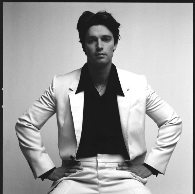 Portrait of an adult male in a suit and button-down shirt, posing in front of a neutral background, photographed in black and white.
