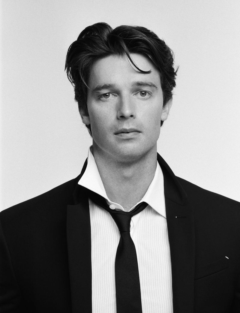 Black-and-white portrait of an adult male in a suit, white shirt, and tie against a clean, bright backdrop in a close-up studio shot.