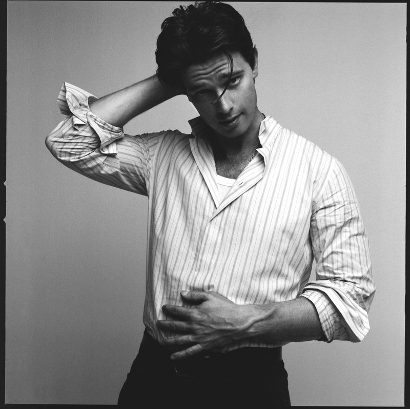 Black and white portrait of a man in a striped shirt with his hand in his hair against a plain background in a photo studio.