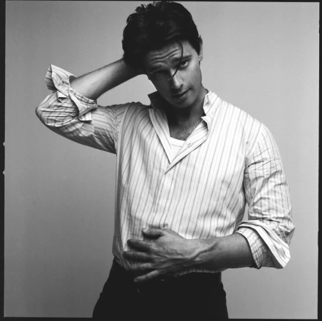 Black and white portrait of a man in a striped shirt with his hand in his hair against a plain background in a photo studio.