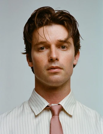Portrait of actor Patrick Schwarzenegger wearing a pinstripe shirt and tie against a plain light background