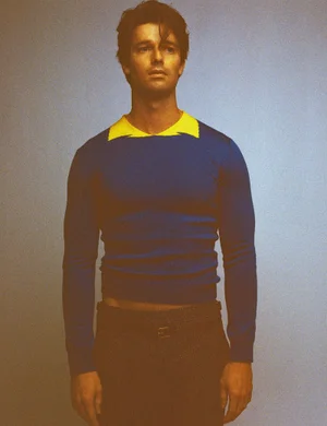 Portrait of actor Patrick Schwarzenegger wearing a blue sweater with a yellow collar for HERO Magazine.