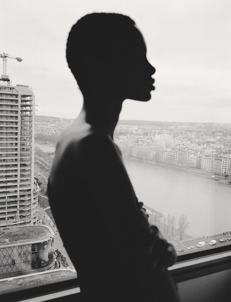 Striking black and white silhouette of a Black woman gazing out over a cityscape, highlighting urban life and the beauty of contemplation.