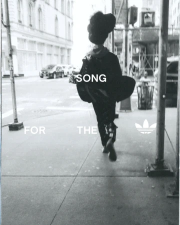 Monochrome street-style image of a person walking away on an urban sidewalk, with Adidas logo, flanked by buildings and parked cars.