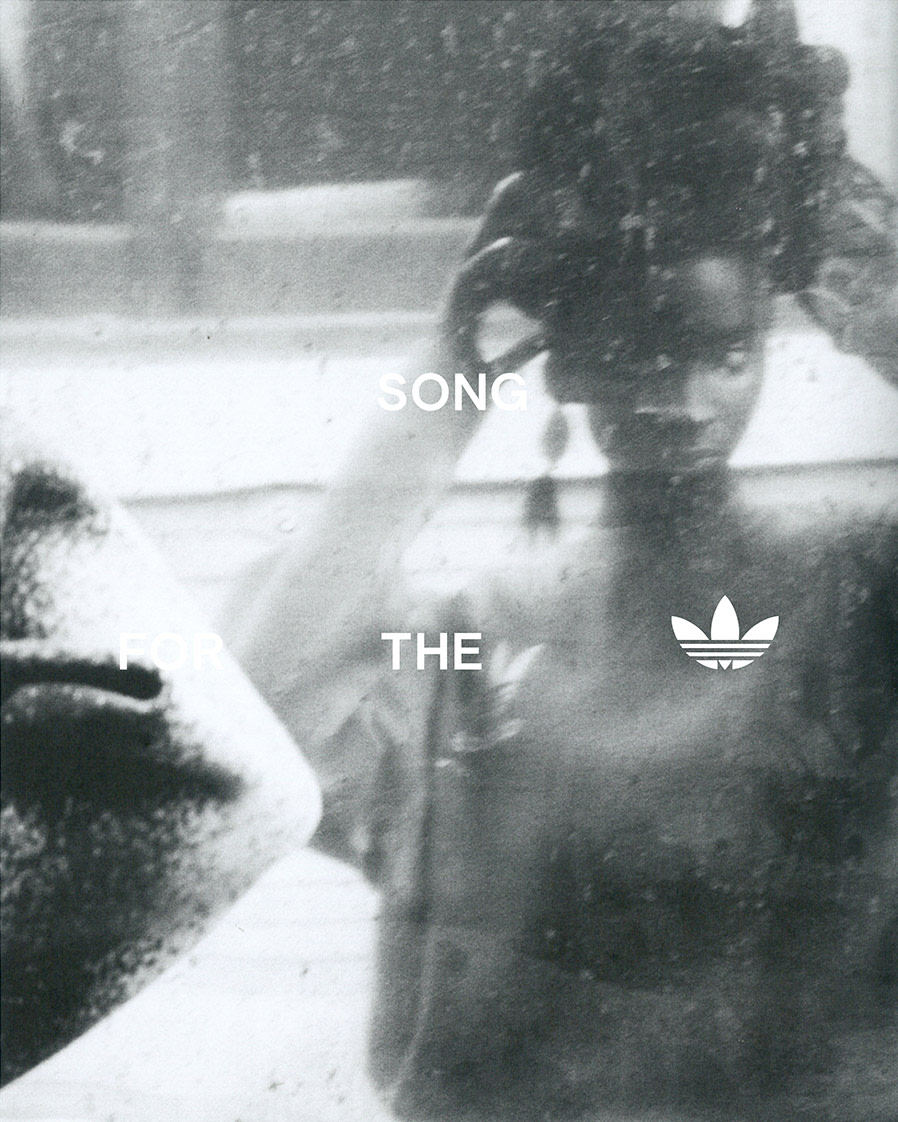 An adult female adjusts her hair in a monochromatic photo with the Adidas logo in the lower right corner, reflected in a mirror.