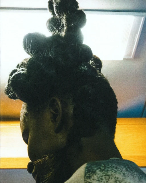 Adult with elaborate updo hairstyle against a yellow background with a soft light, showcasing a contemporary beauty and style.