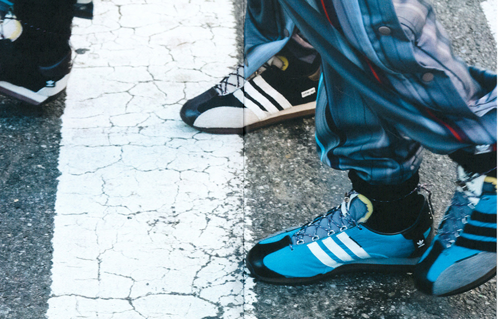 Two pairs of Adidas sneakers, in blue and black, worn on a crosswalk, showcasing vintage style and athletic footwear.