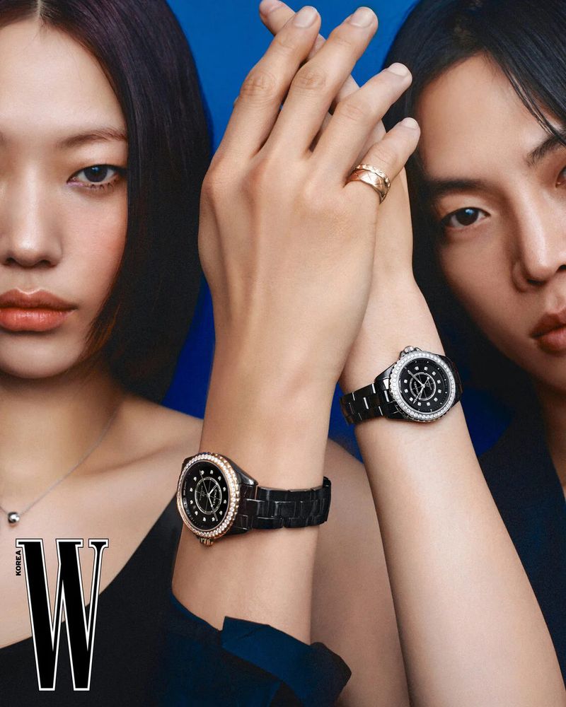 Two Asian adults showcase black ceramic watches with jeweled bezels, gold ring, against a blue background with a fashion magazine cover.