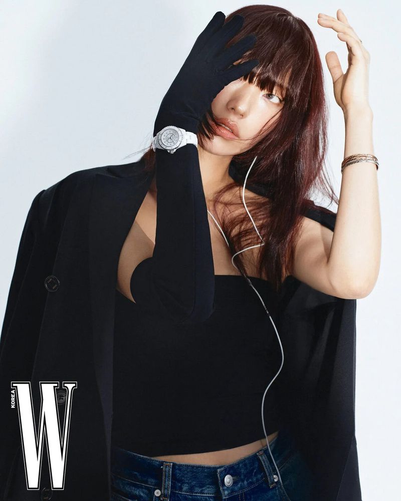 Glamorous portrait of a woman with dark hair, wearing a black top and jeans, accessorized with a watch and bracelets, against a white background.