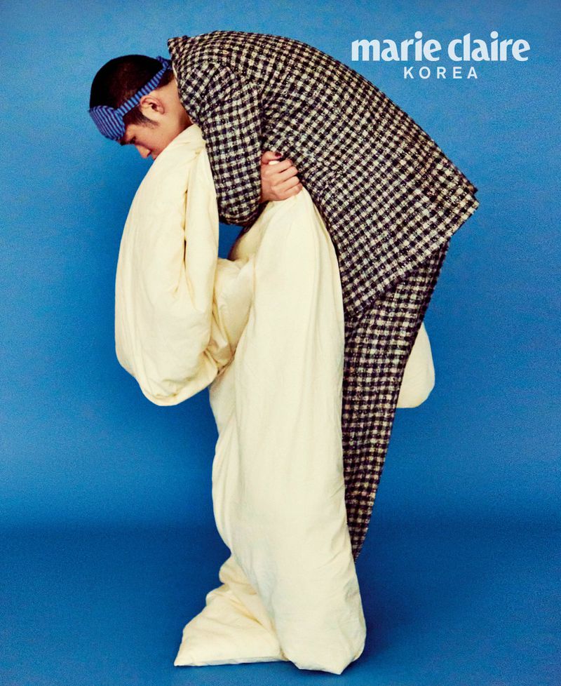 Adult male wearing a pajama set and blue eye mask poses with a duvet on a blue background for Marie Claire Korea fashion editorial.