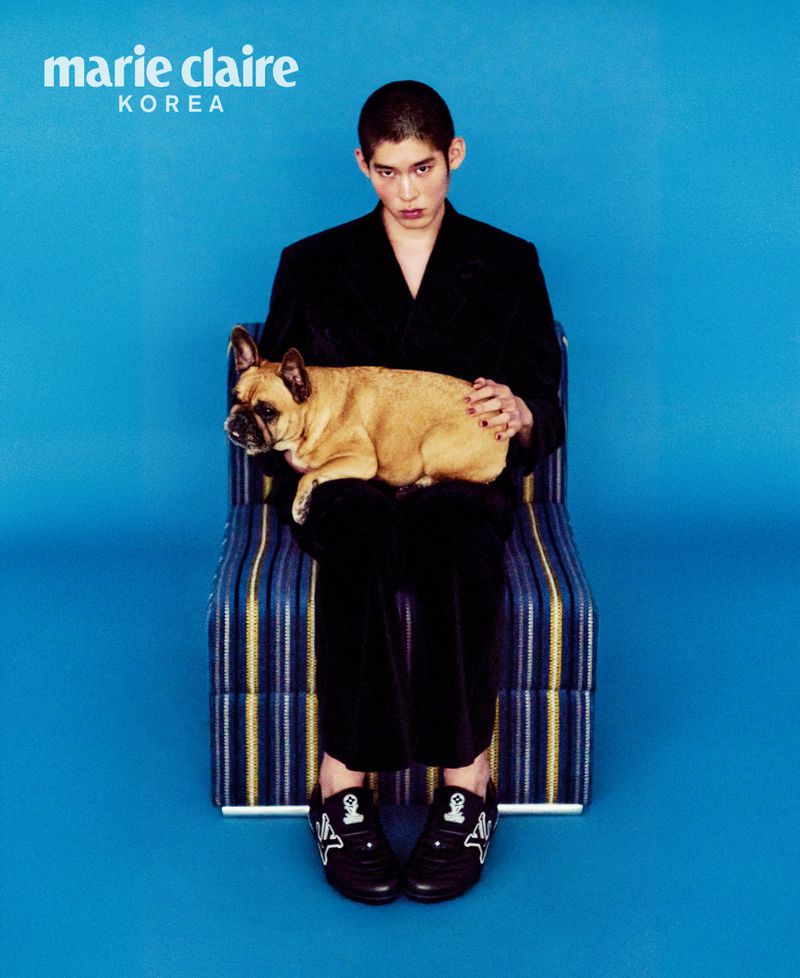 Adult male in a black suit seated holding a light-brown French bulldog against a blue background, published in Marie Claire Korea.