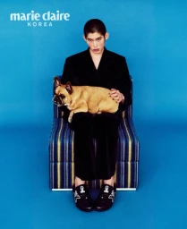 Man seated on a striped armchair against a blue background, holding a fawn French bulldog on his lap.