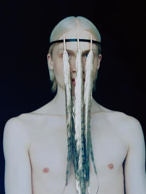 Portrait of a shirtless man wearing a headband with three hanging feathers obscuring his face