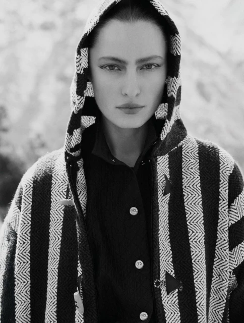Monochrome portrait of a woman with a hooded jacket, mountain background. Black and white fashion photography with a natural outdoor setting.