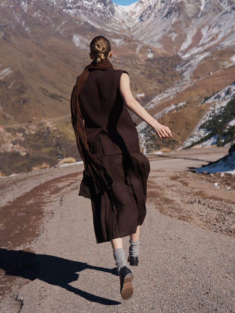 Model in brown sleeveless top and skirt with scarf running on mountain road