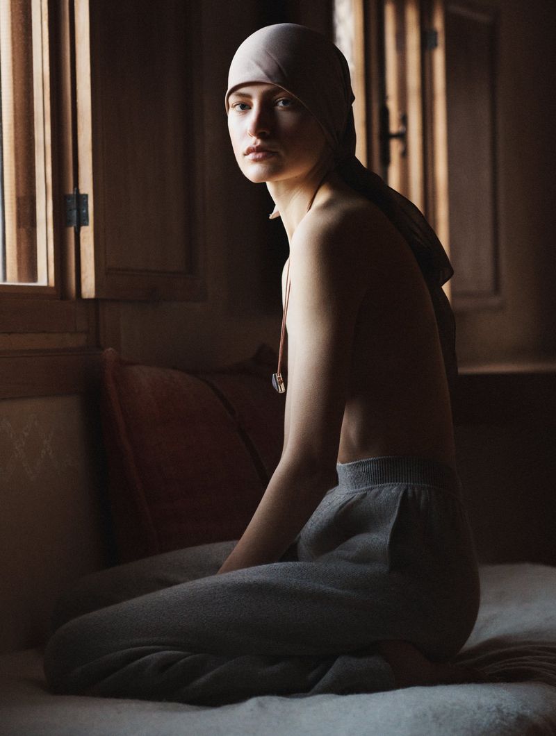 Striking portrait of a young woman in a headscarf, seated in soft light against a dark background, showcasing a blend of fashion and fine art.