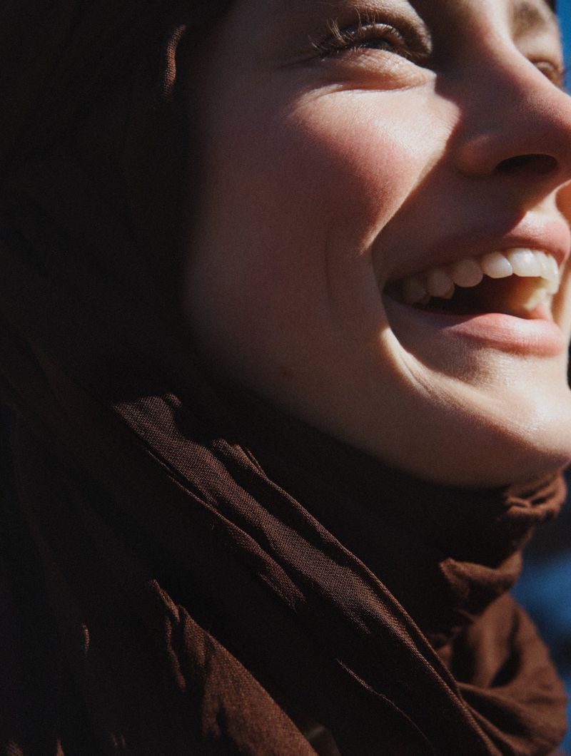 Close-up portrait of a happy adult woman smiling in outdoor daylight, wearing a brown scarf.  Head and shoulder shot, warm lighting.