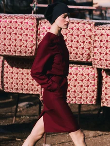 Model Felice Nova Noordhoff in a burgundy dress and black cap walking past patterned cushions