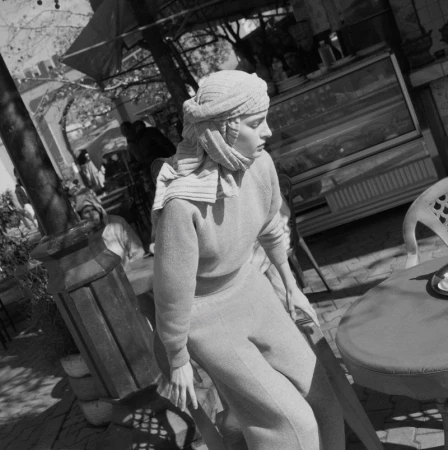 Model Felice Nova Noordhoff wearing a wrapped headscarf and knit outfit seated outdoors in a black and white editorial photograph.