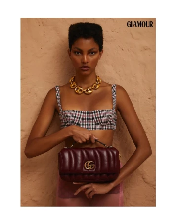 Glamour editorial fashion shot: a model poses with a Gucci handbag against a beige background, showcasing a stylish and sophisticated aesthetic.