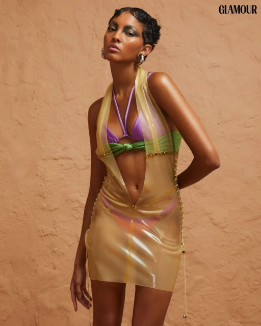 Fashion editorial shot featuring an adult female model in a yellow mini dress, posing in a studio setting against a textured wall backdrop.