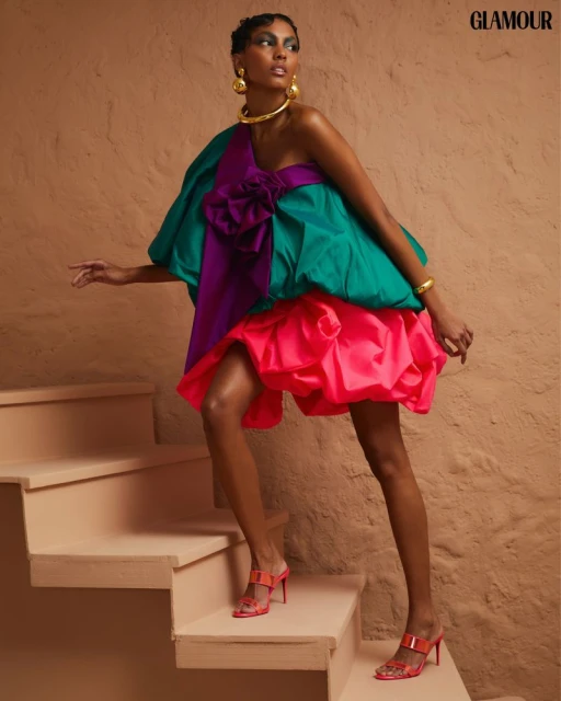 Fashion editorial shot of an African-American woman in a voluminous dress and high heels, walking on a staircase in a photo studio.