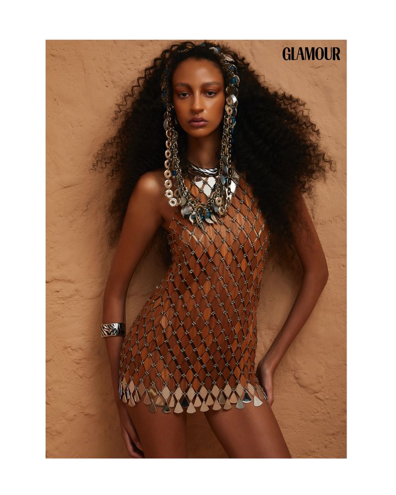 Glamour magazine editorial image featuring a Black woman with long curly hair wearing a chainmail dress and statement jewelry.