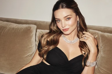 Miranda Kerr wearing a diamond necklace and bracelet in a black dress seated against a cushioned sofa