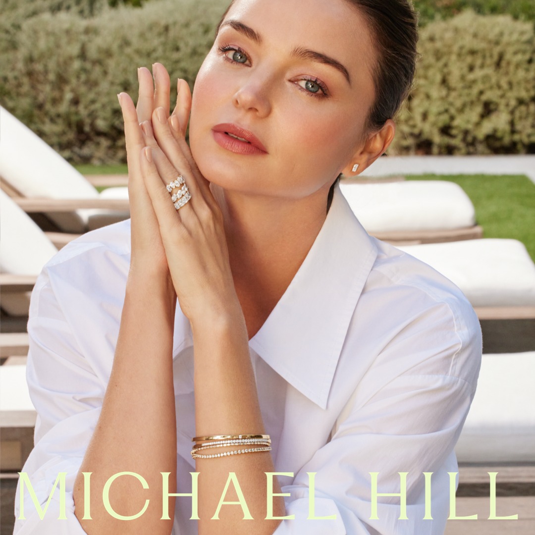 Close-up of adult female model with blonde hair wearing white button-down shirt and jewelry outdoors in a bright setting.