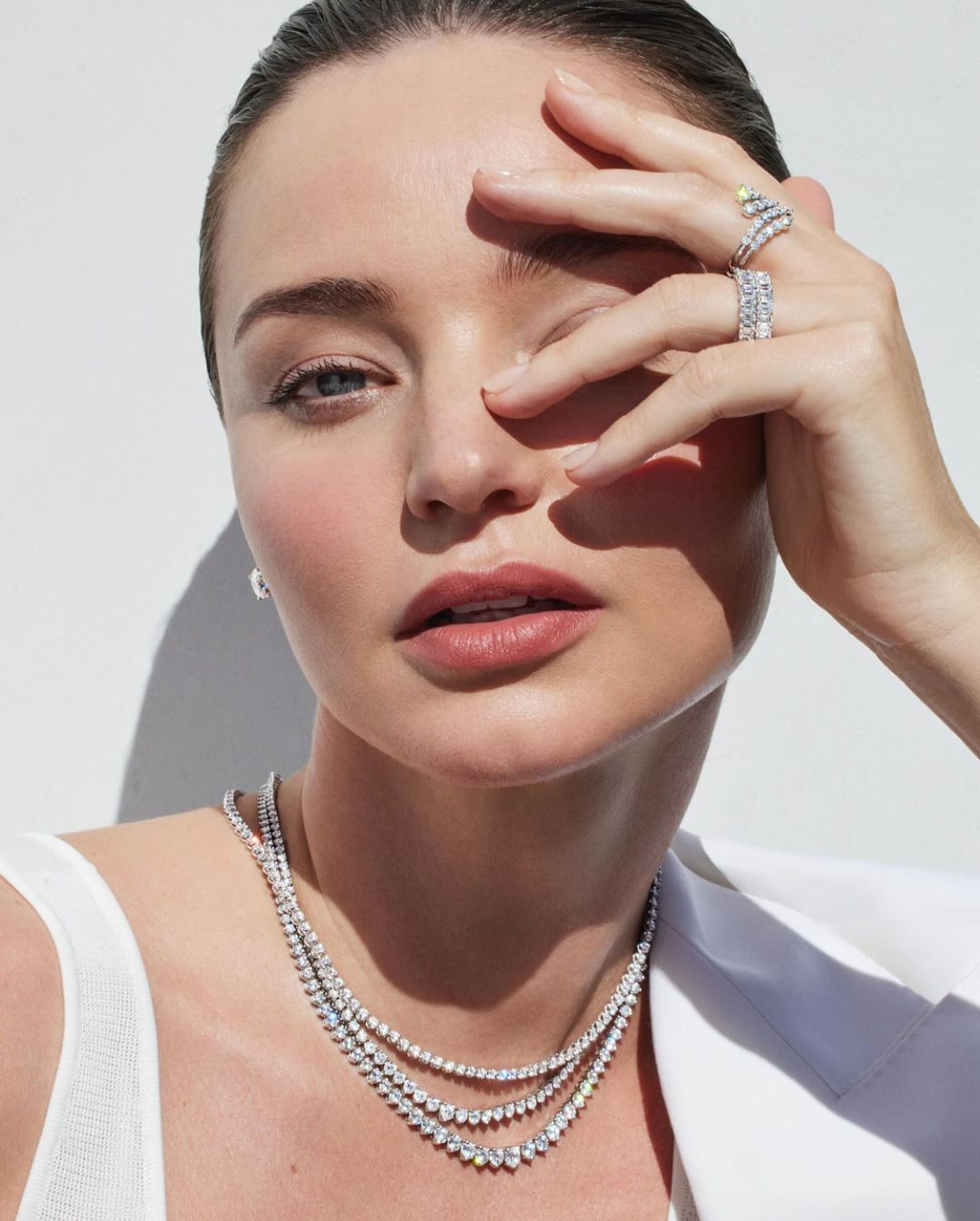 Close-up of a fair-skinned adult woman with jewelry covering her face and neck, against a bright white background.
