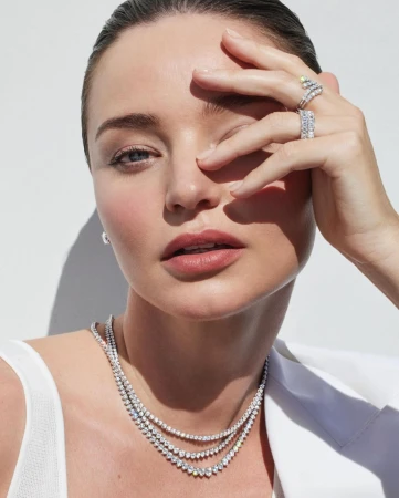 Close-up of a fair-skinned adult woman with jewelry covering her face and neck, against a bright white background.