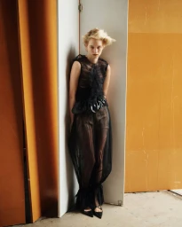 Model in a black sheer dress standing between wooden panels for SSAW Magazine
