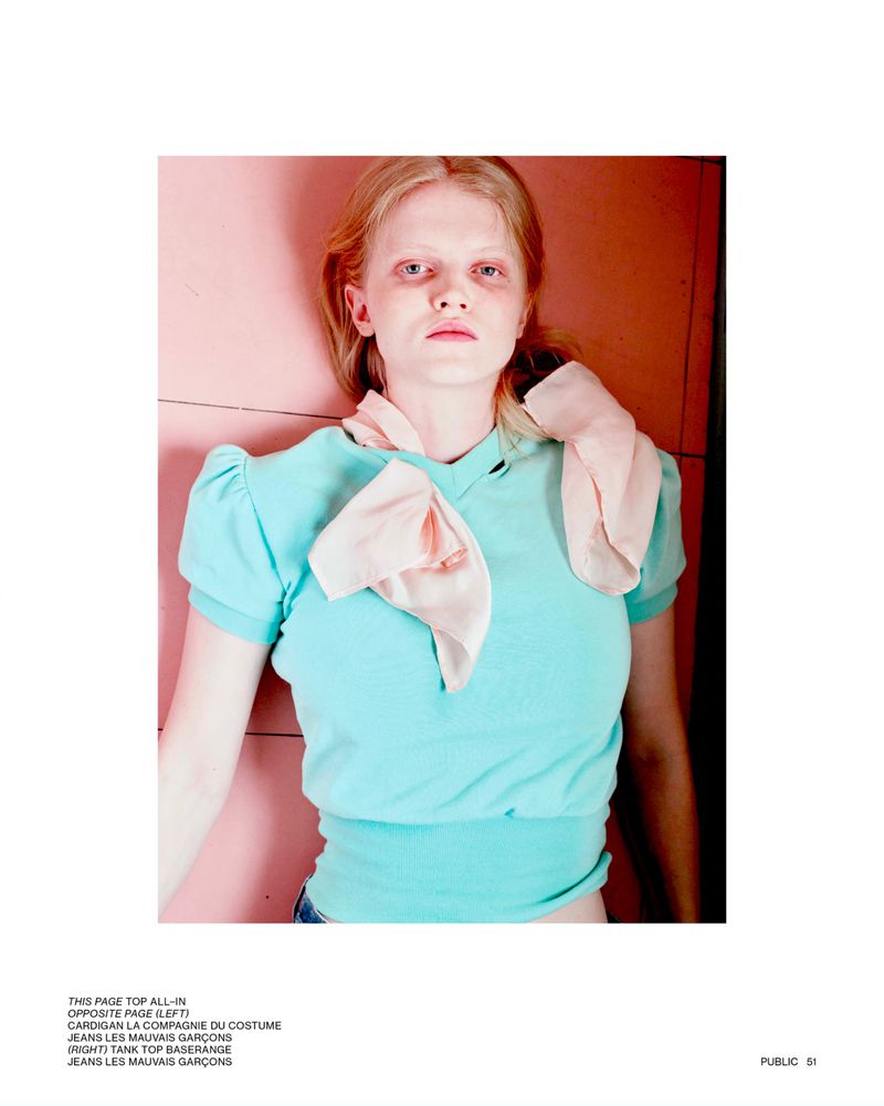 Young woman in a blue short-sleeve blouse with a pink scarf, lying against a pink background, fashion editorial, medium shot.